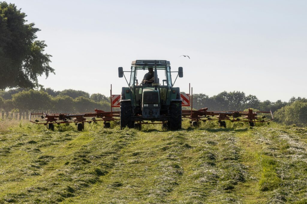 A tractor operates in a sunny rural field, plowing farmland for harvest season.